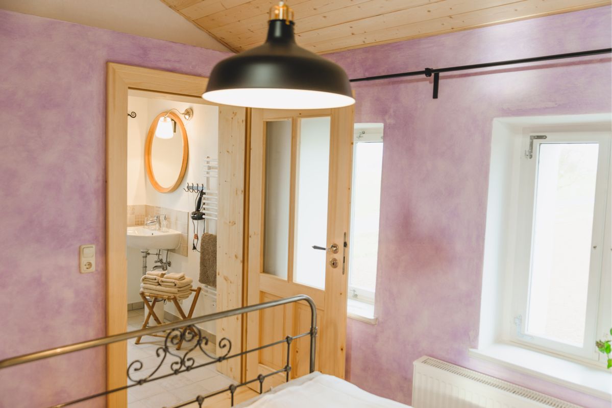 Violett gestrichenes Schlafzimmer mit geöffneter Tür zum angeschlossenem Badezimmer