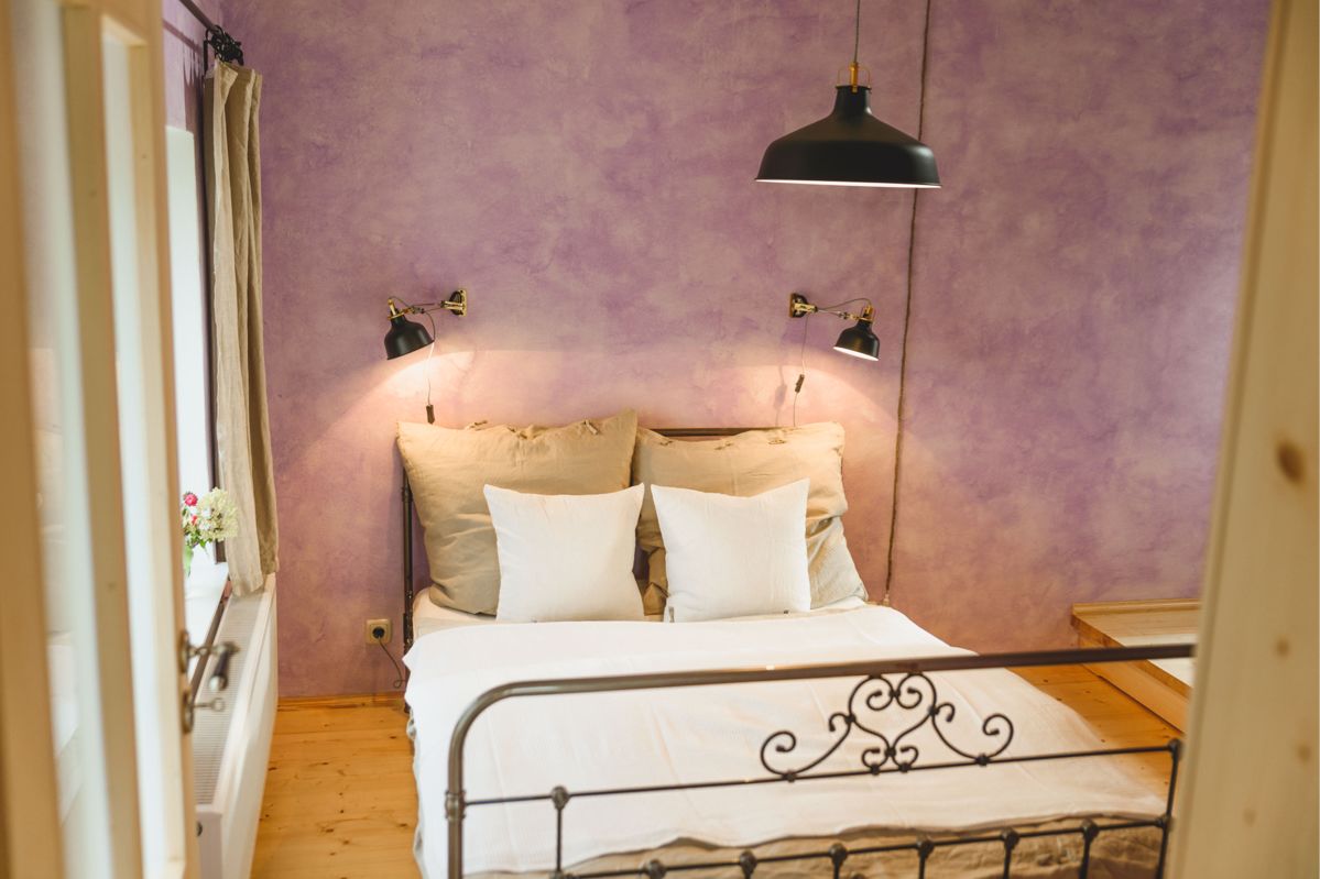 Einblick in ein Schlafzimmer, zu sehen ein Doppelbett an einer violetten Wand