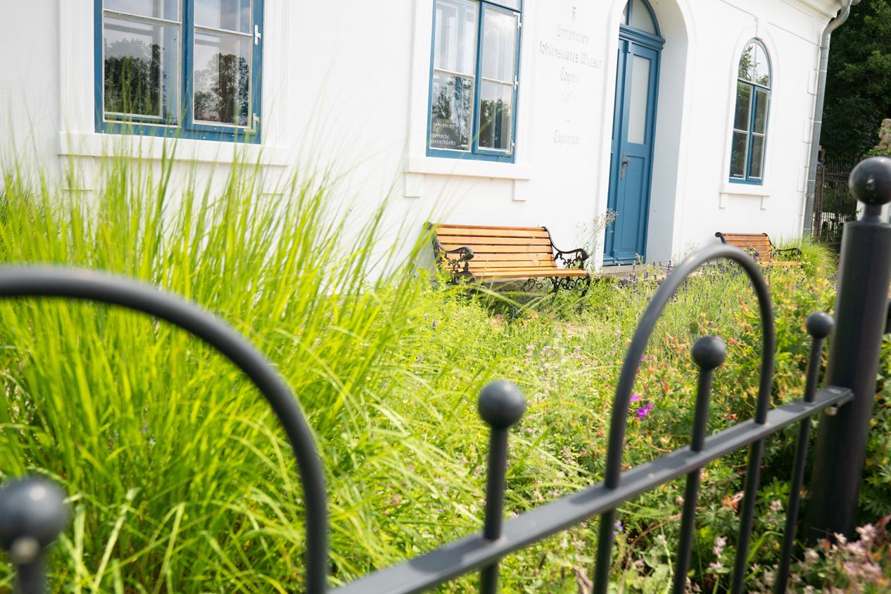 Ferienhaus Alte Wasserschänke mit Vorgarten und zwei Bänken, im Vordergrund Zaun aus Metall